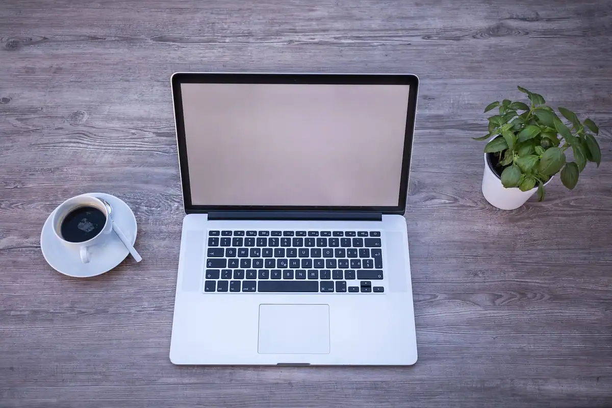 Laptop deschis pe un birou, lângă o ceașcă de cafea, pregătit pentru actualizările sistemului