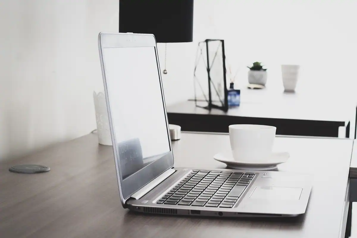 Laptop deschis pe un birou alb, cu o ceașcă alături, pentru lucru concentrat în browser