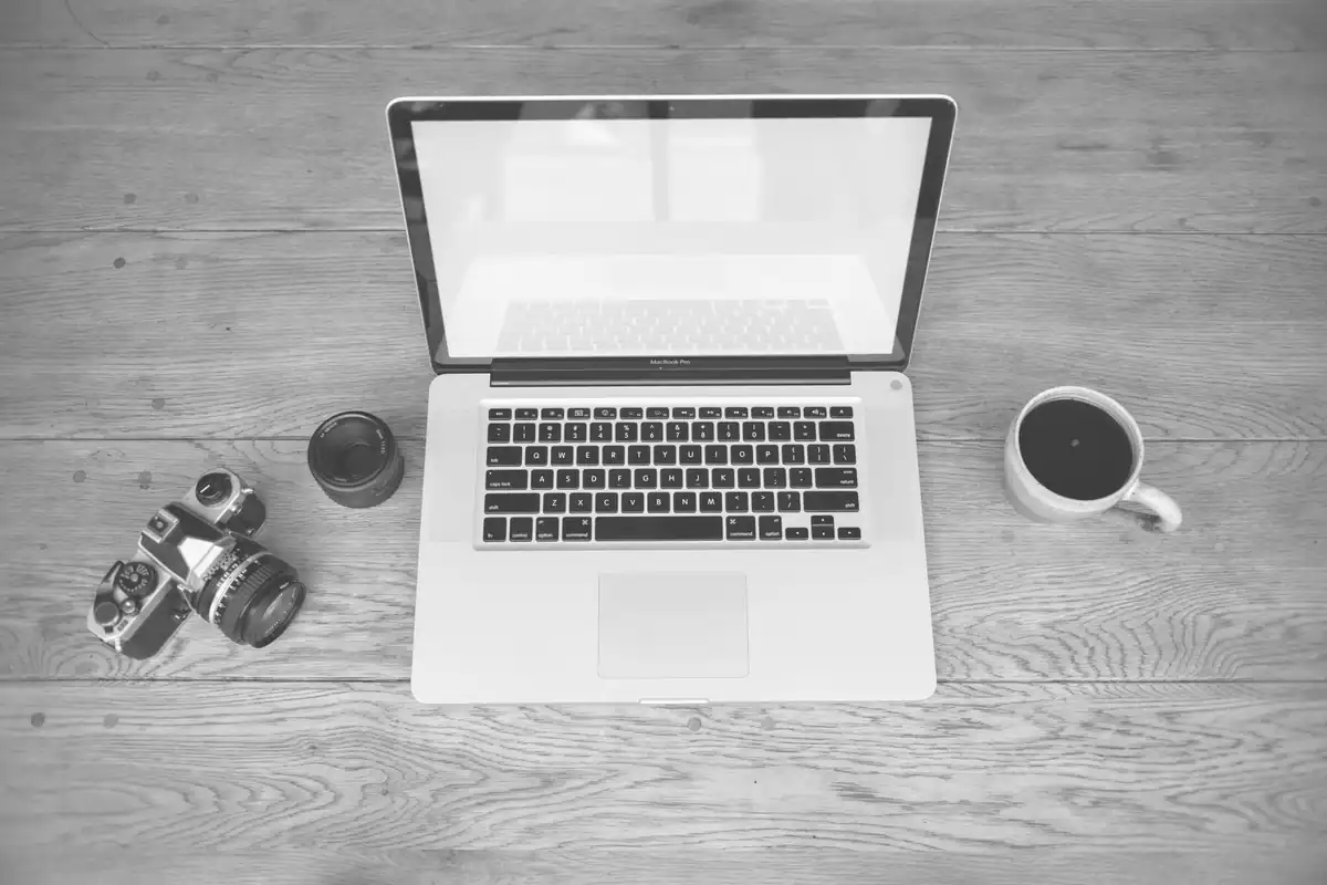 Laptop deschis în alb-negru pe o masă, lângă o cafea și mici obiecte