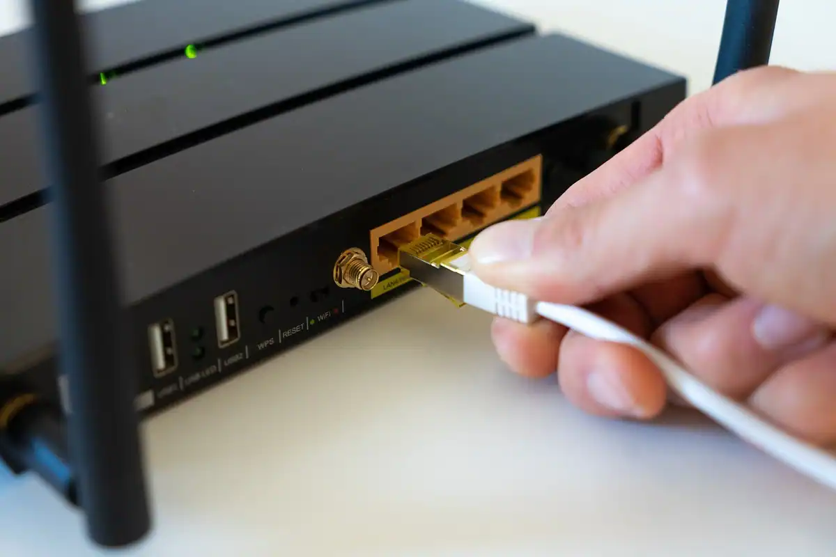 Mână care introduce un cablu de rețea alb într-un router negru cu antene