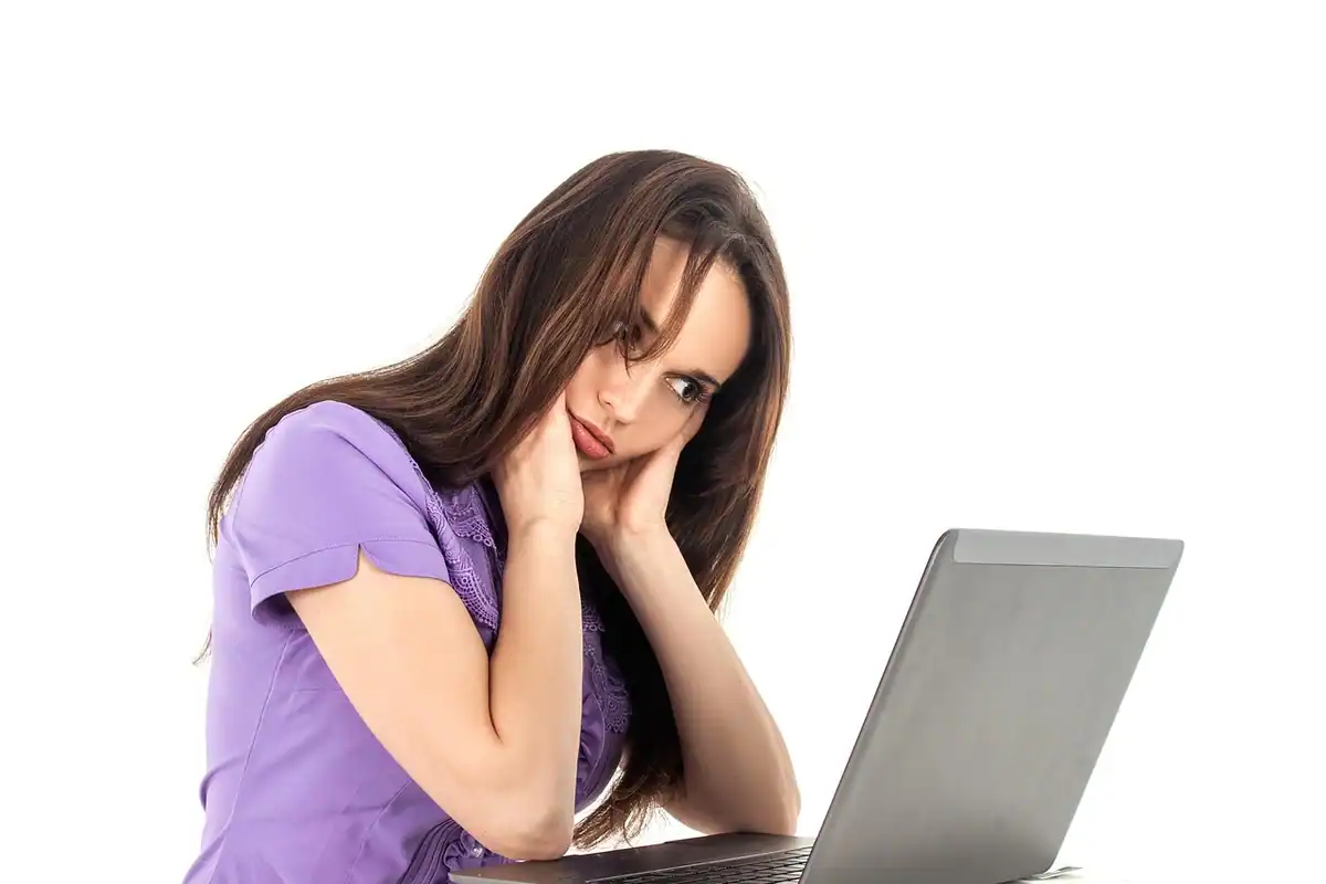 Femeie obosită, cu mâinile la față, așezată în fața unui laptop prea lent