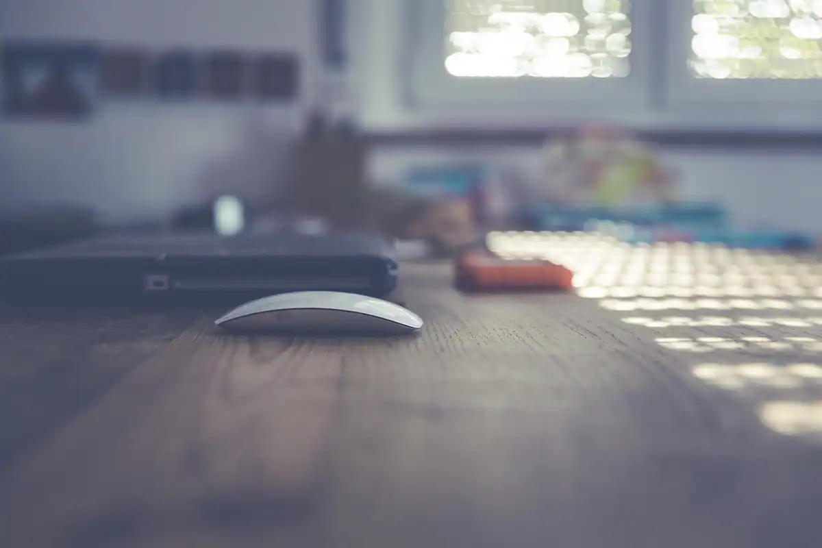 Mouse alb pe un birou luminos, fotografiat din apropiere, într-o cameră liniștită