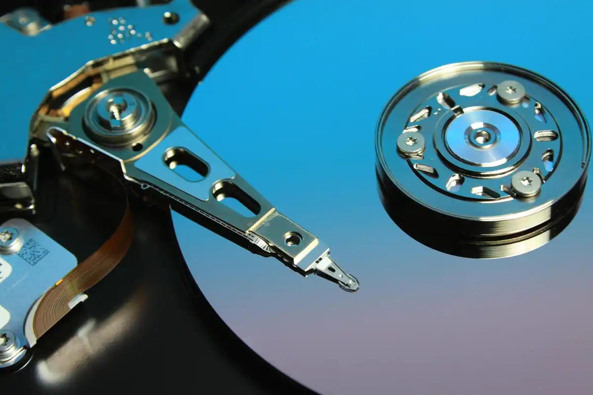 Hard disk deschis, cu brațul de citire deasupra unui platan albastru lucios