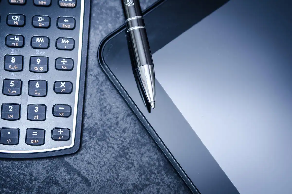 Calculator de birou cu butoane numerice, alături de un pix și o tabletă