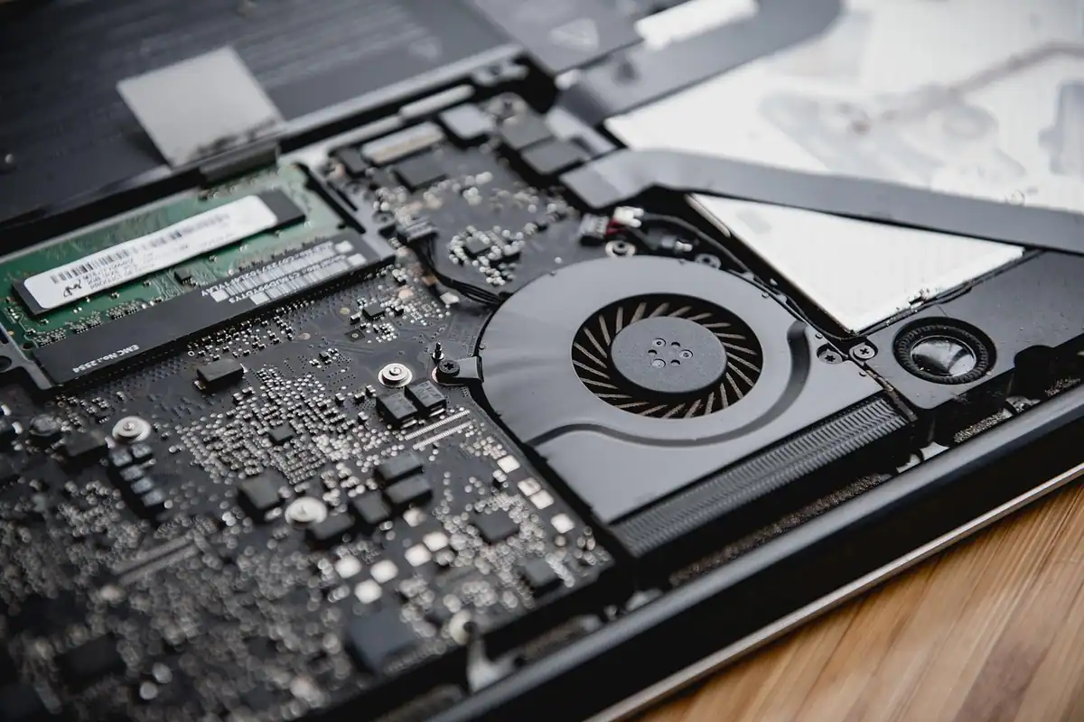 Interiorul unui laptop desfăcut, cu ventilator, memorie RAM și placa de bază la vedere
