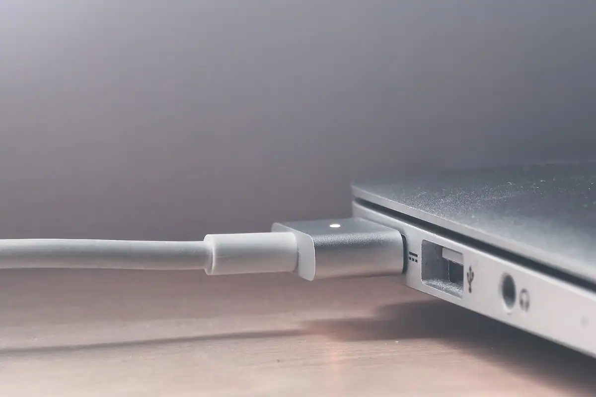 Cablu de încărcare alb conectat la un laptop argintiu, pentru verificarea bateriei