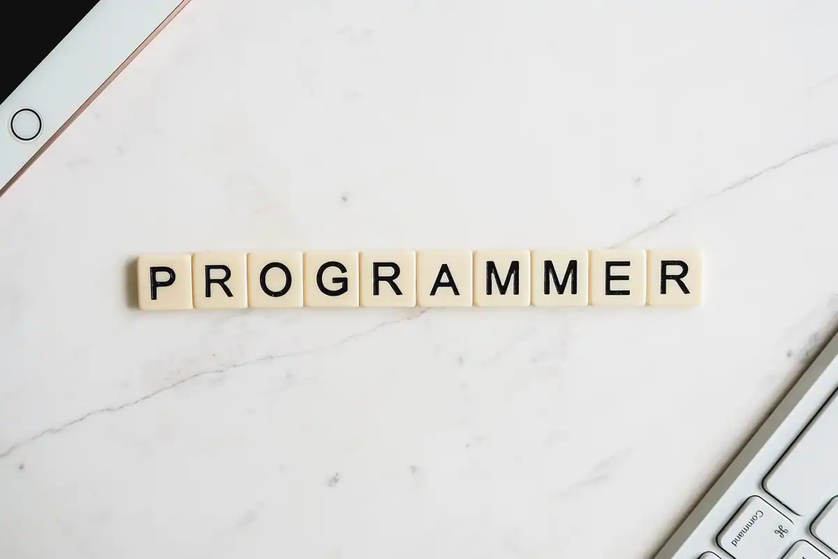 Litere de joc de societate formând cuvântul programator, lângă tastatura unui laptop