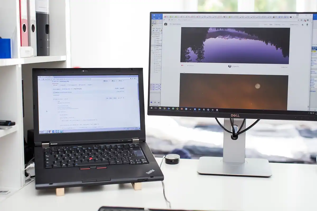 Laptop deschis lângă un monitor mare, pe un birou alb dintr-un birou acasă