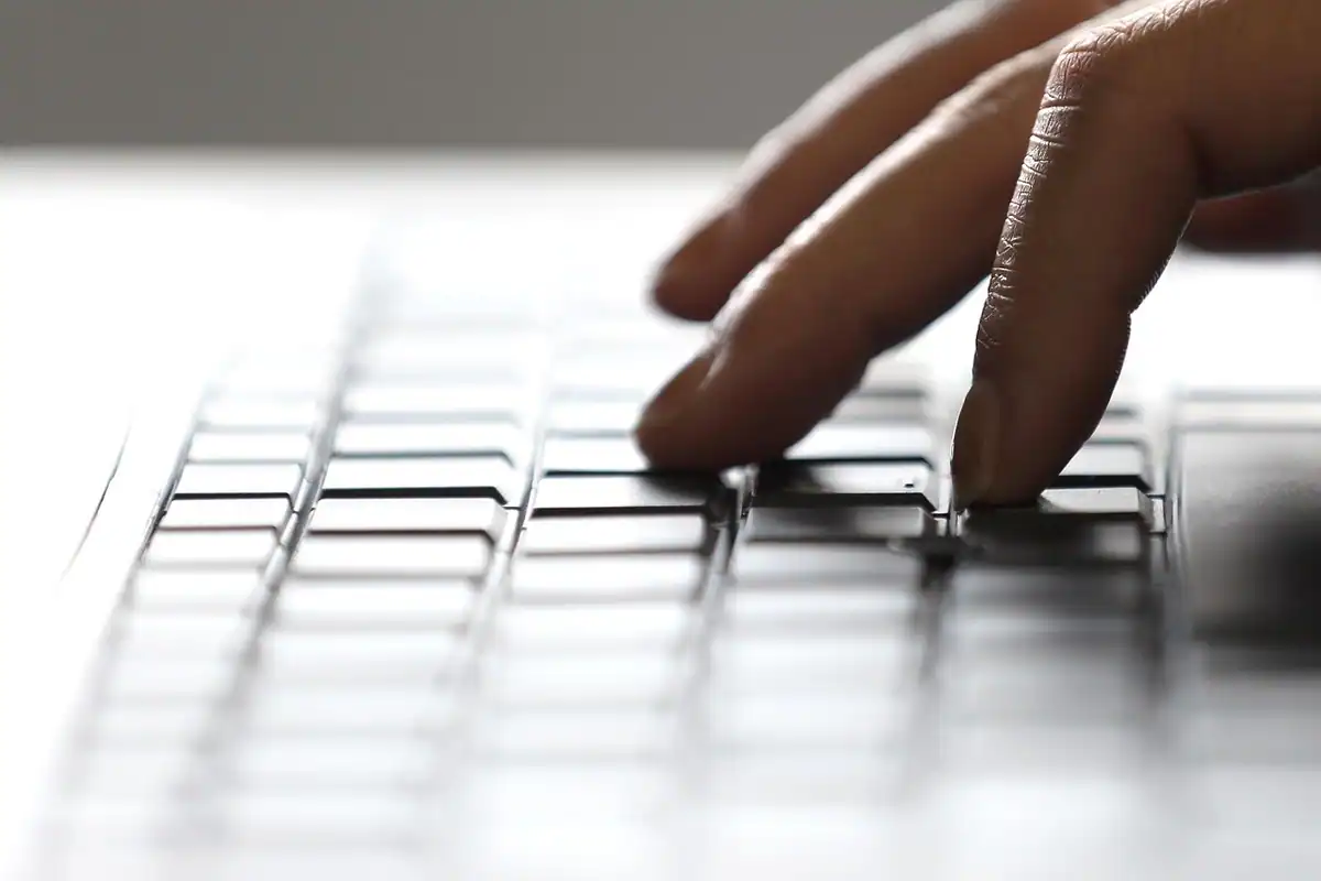 Degete care apasă tastele unui laptop cu tastatură deschisă la culoare