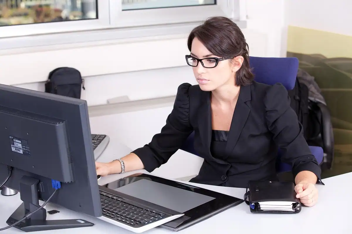 Femeie cu ochelari care lucrează la un monitor și la o tabletă grafică, la birou