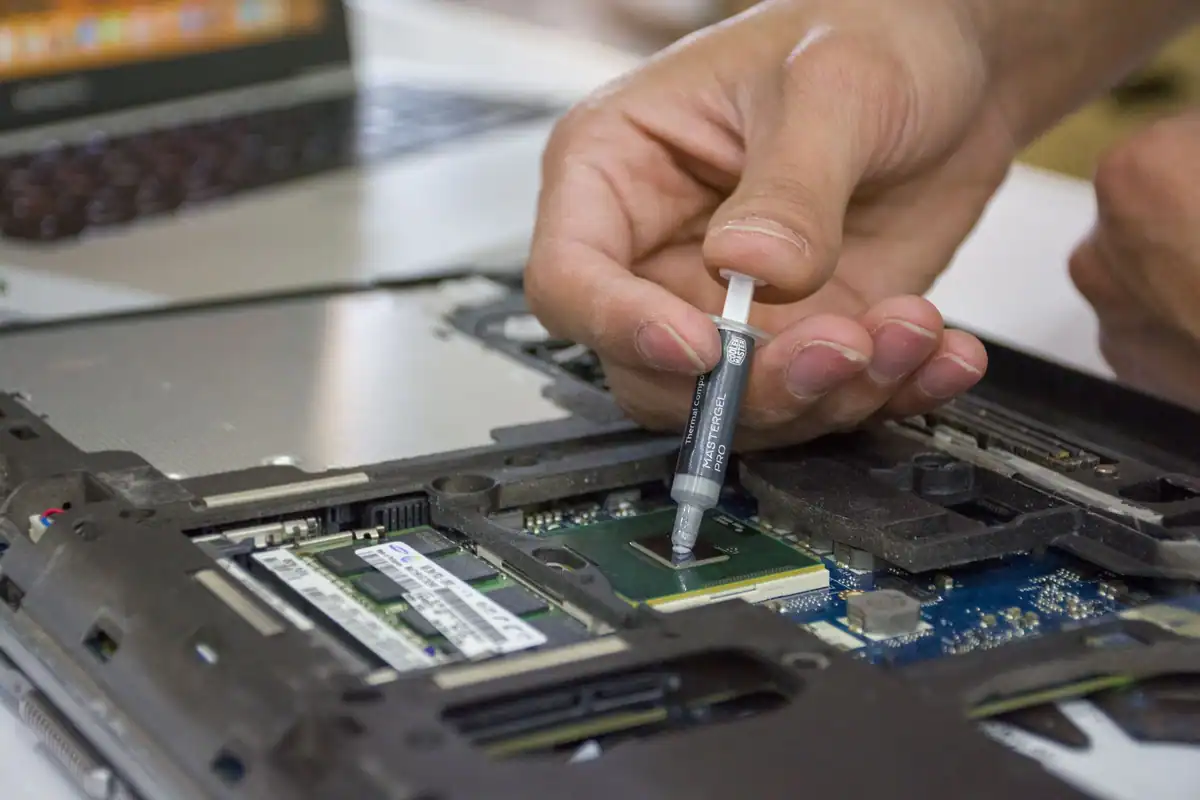 Mână care aplică pastă termoconductoare pe un procesor de laptop, în plan apropiat