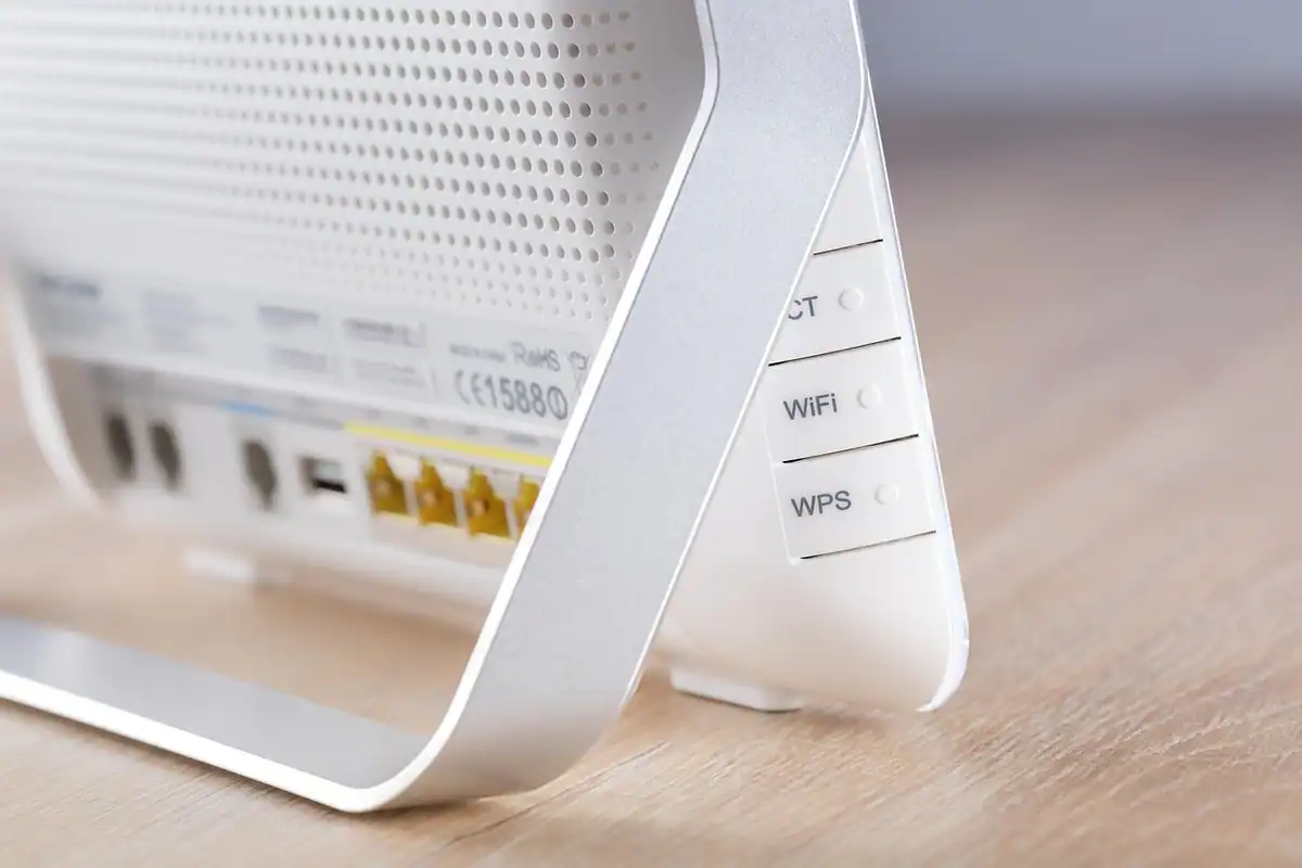 Router alb Wi-Fi cu porturi galbene și butoane, așezat pe o masă din lemn