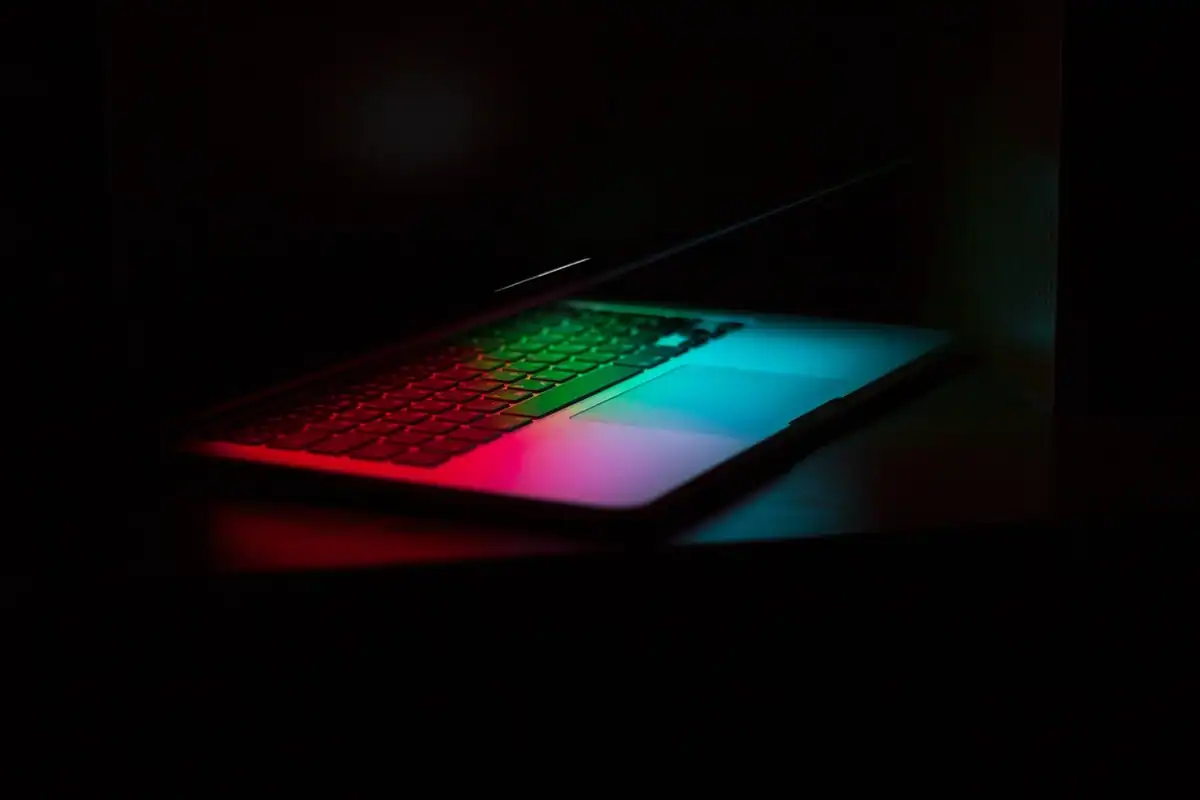 Laptop în întuneric, cu tastatura luminată în verde, roșu și albastru