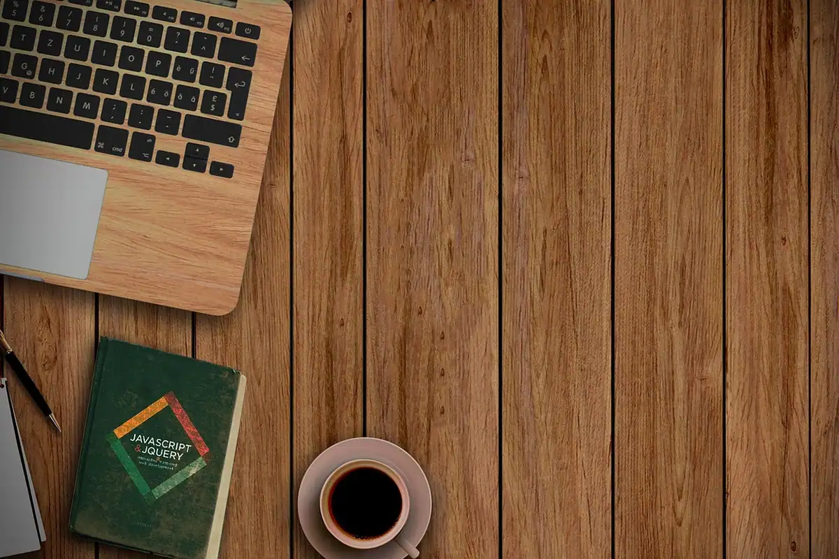 Birou din lemn cu colțul unui laptop, o ceașcă de cafea și o carte verde