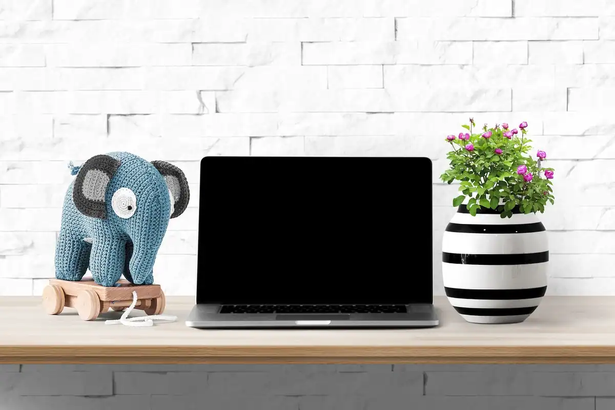 Laptop cu ecran stins, un elefant de pluș și o vază cu flori pe un birou