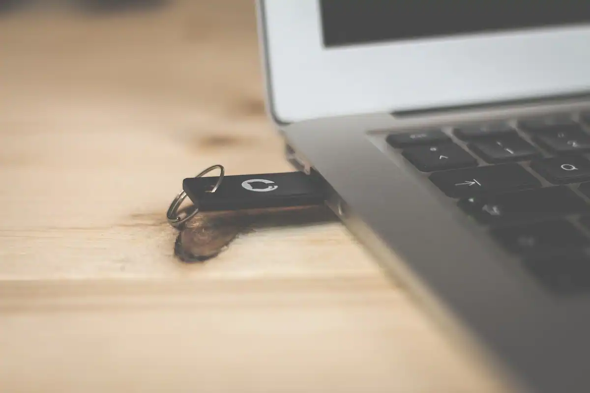 Stick de memorie mic negru, lăsat pe masă lângă marginea unui laptop argintiu